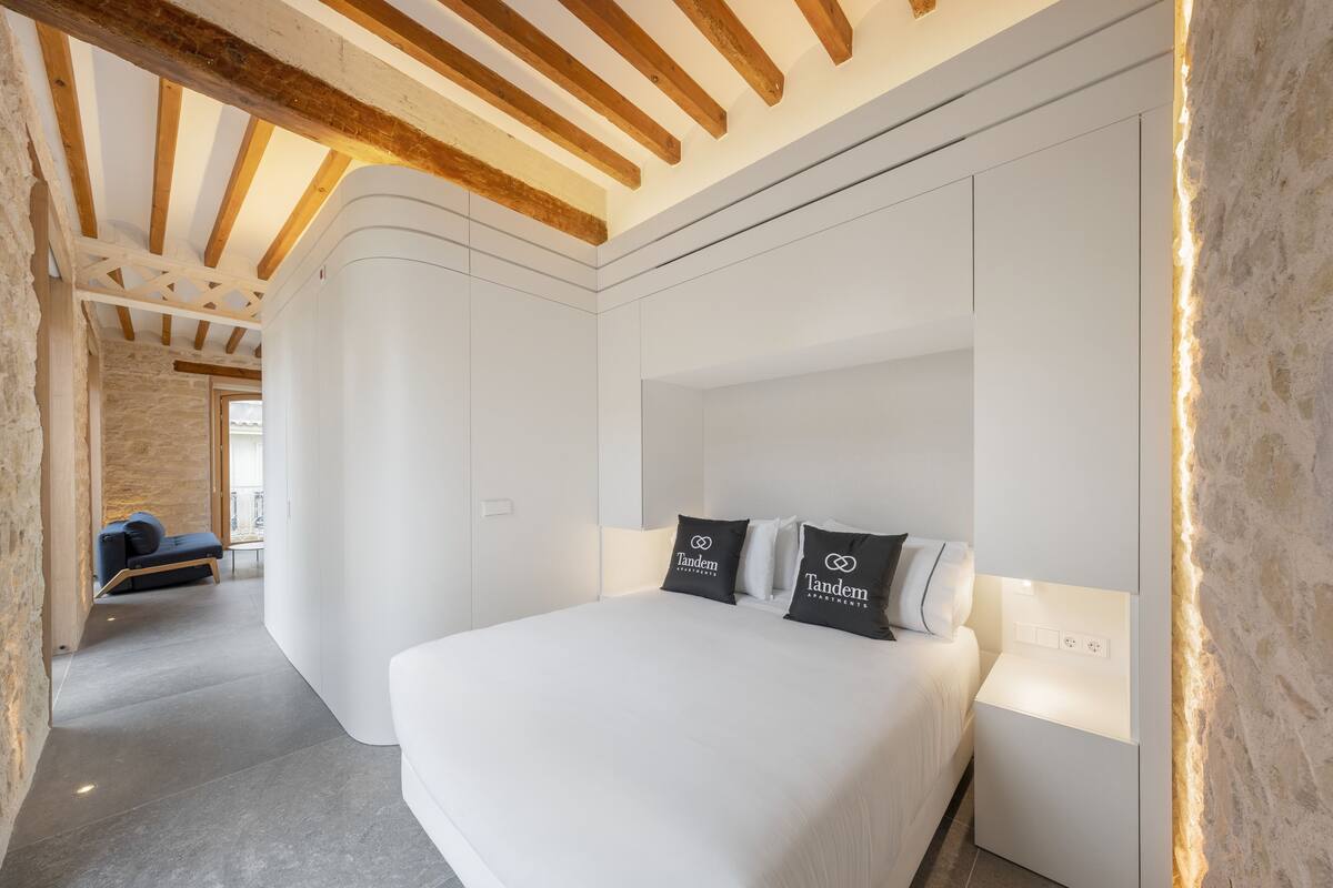 Een moderne slaapkamer met een groot bed, witte muren en zichtbare houten balken.