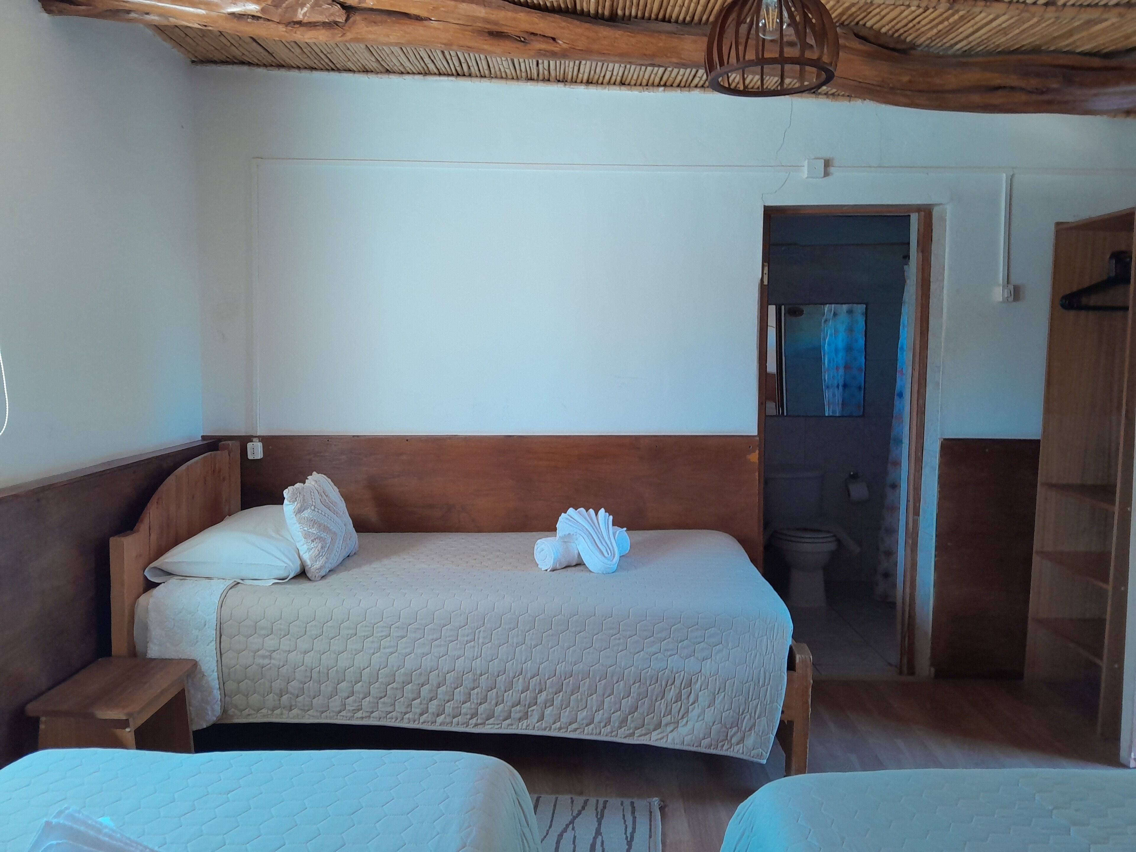 A bedroom with two beds, wooden headboards, a woven ceiling, and a visible bathroom door.