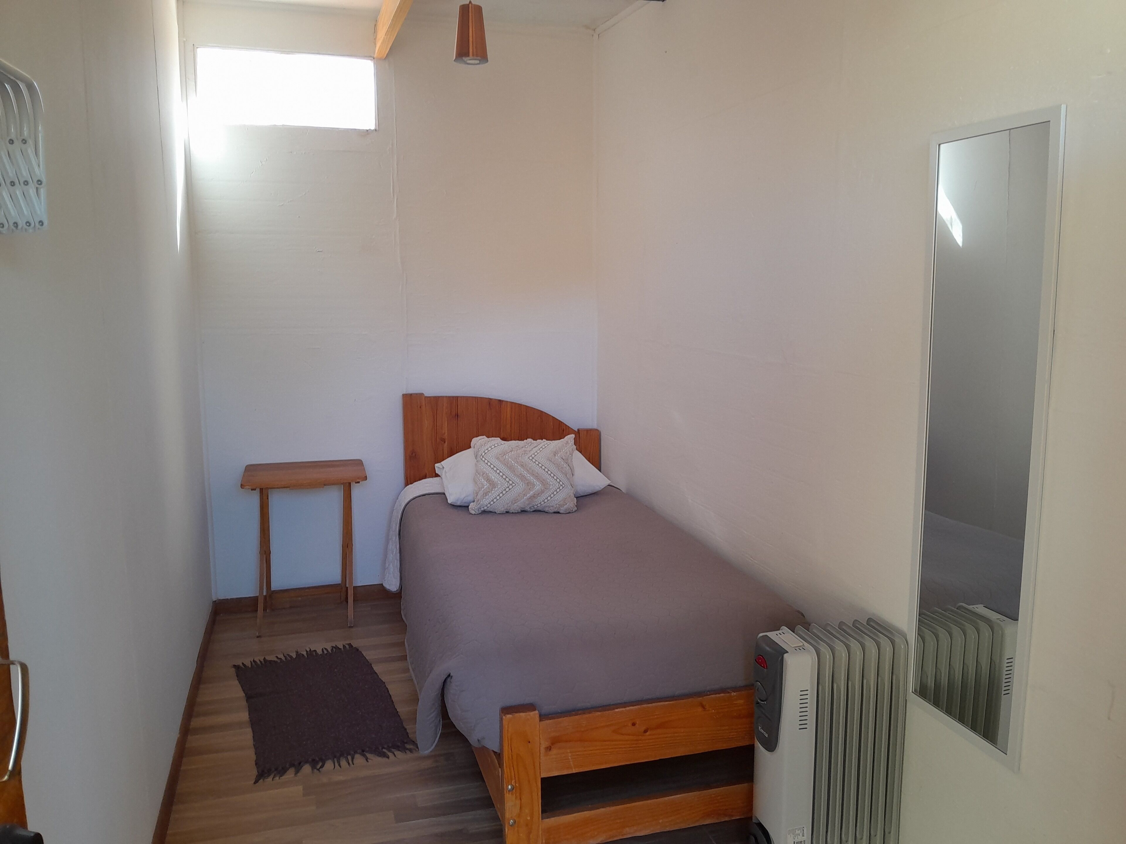 Et lille, smalt værelse med en enkelt seng, et trænatbord, et lille bord og en radiator.