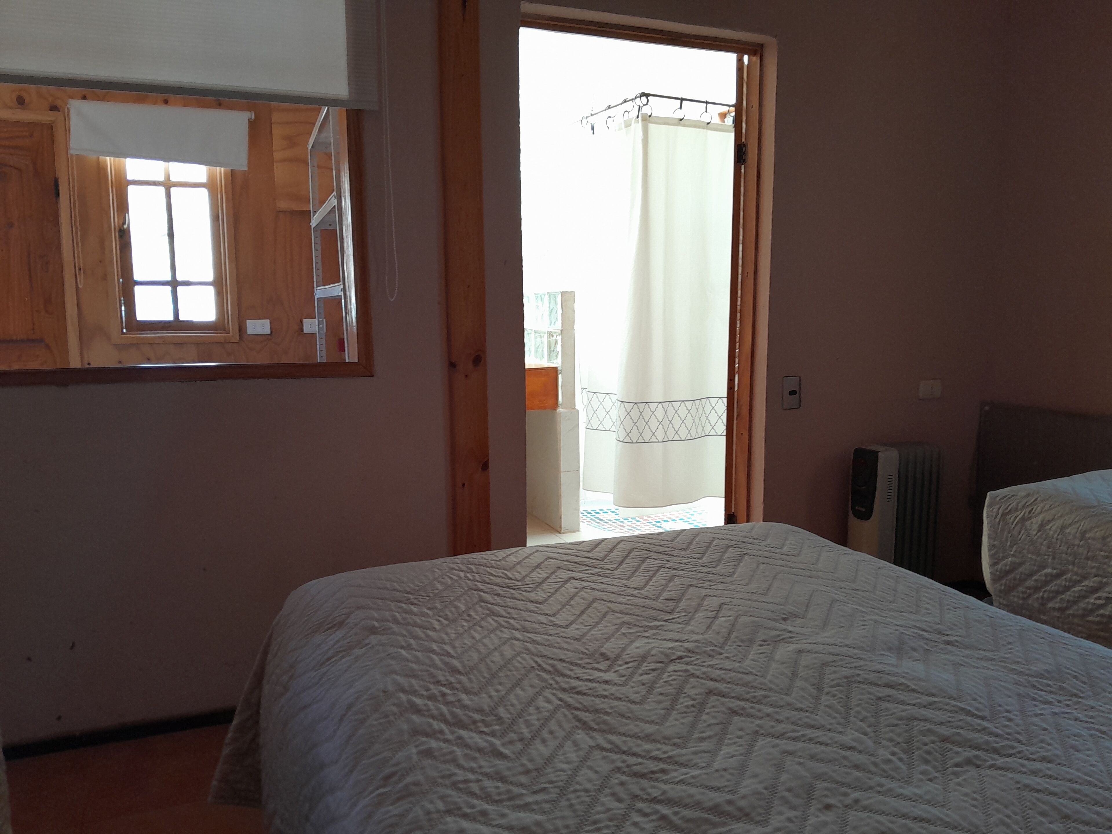 Une chambre avec un grand lit, une fenêtre avec un cadre en bois et un radiateur.