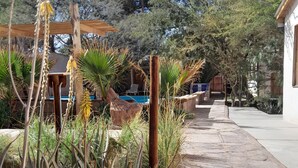 Un jardín con piscina, rodeado de plantas y una pérgola de madera.