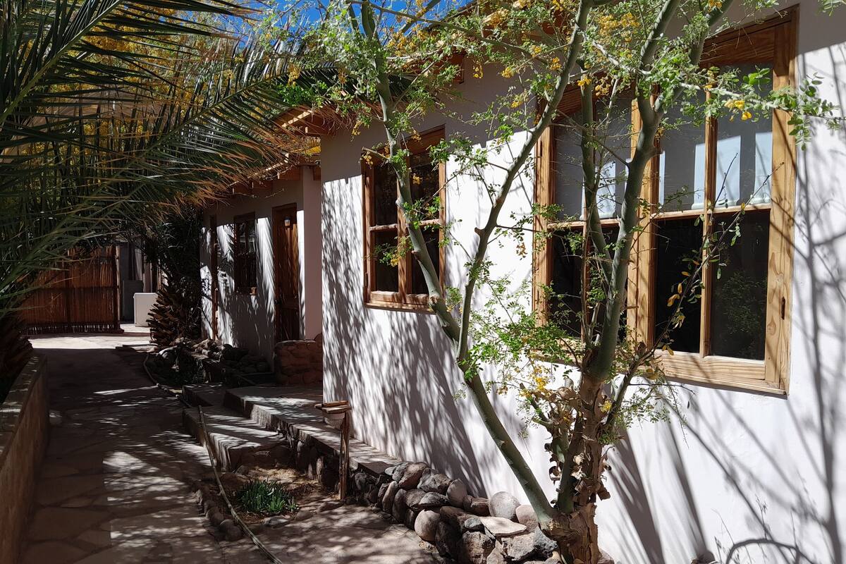 Un estrecho sendero de piedra que lleva a un edificio blanco con ventanas de madera y estructura de techo de paja.