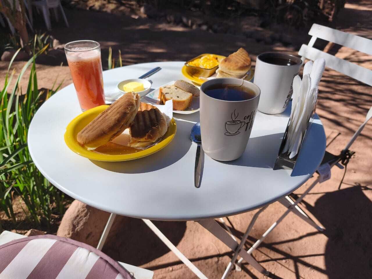 Une table ronde avec un repas composé de pain, de beurre, une boisson et des tasses de café.