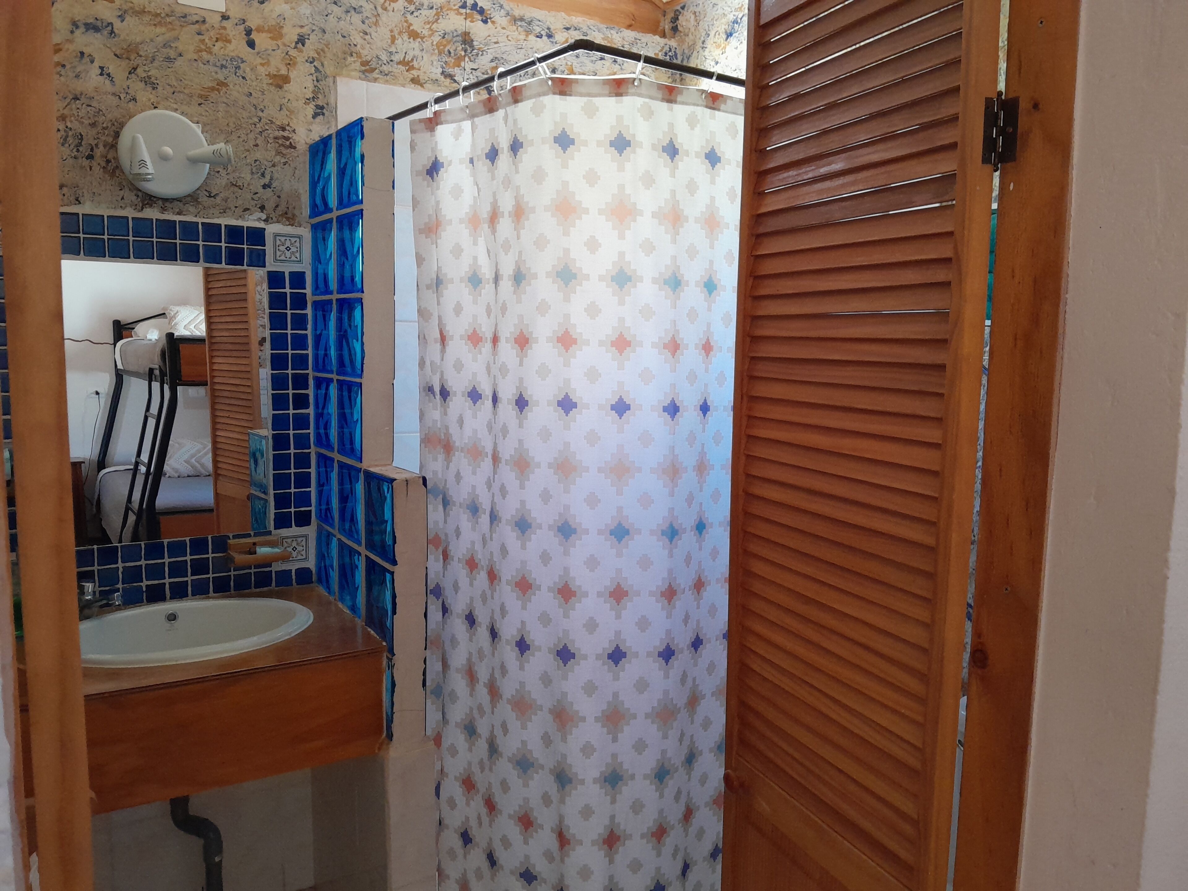 Un baño con lavamanos, espejo, cortina de ducha y persianas de madera.