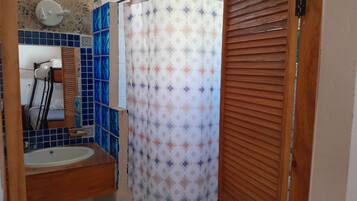 Un baño con lavamanos, espejo, cortina de ducha y persianas de madera.