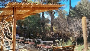 Un área de estar al aire libre con mesas y sillas de madera, un banco de madera y una estructura de pérgola.