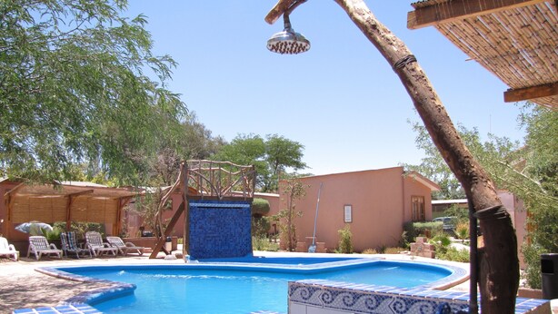 Una piscina con borde de mosaico azul, una estructura de madera en la parte superior y un techo de paja cerca.