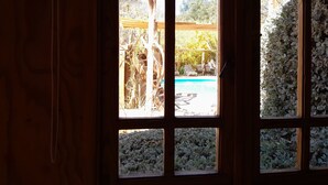 Vista a través de una ventana de paneles múltiples, que muestra una zona de piscina con sillones de descanso y una pérgola.