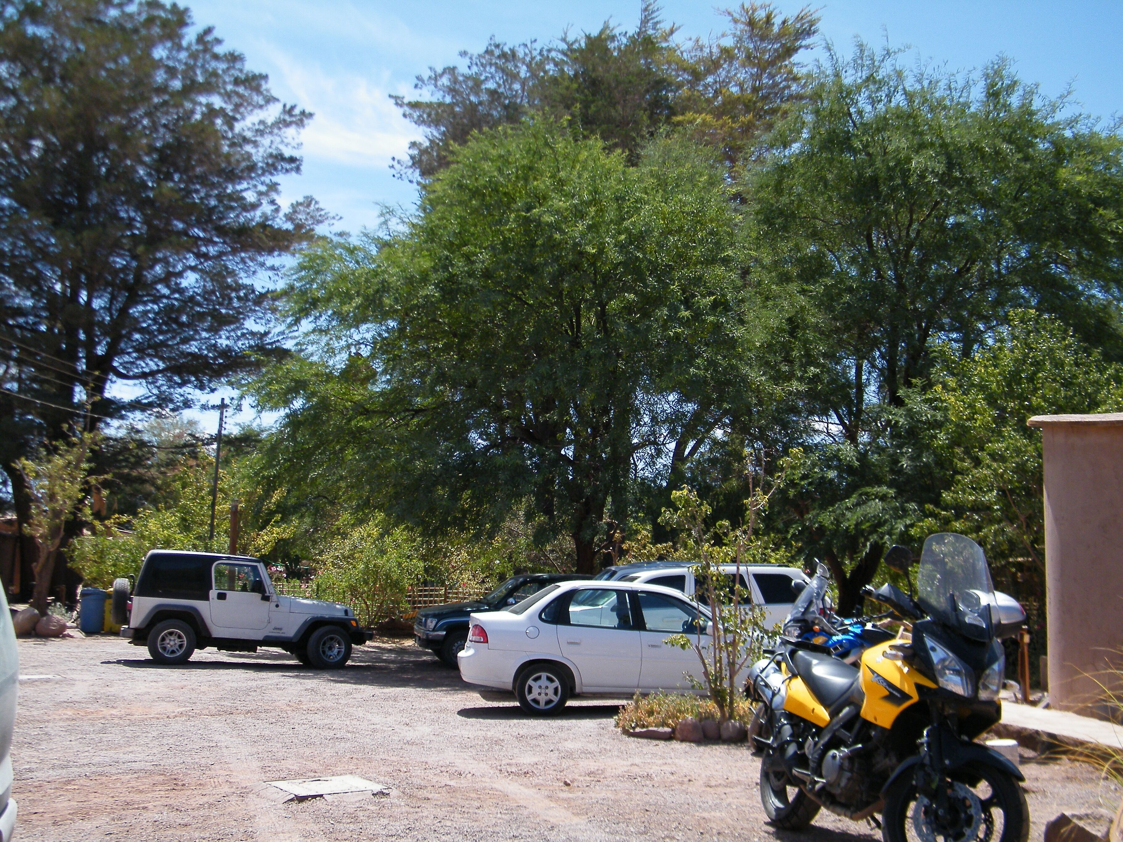 A parking area with several vehicles, including a white SUV, a white sedan, and a yellow motorcycle.
