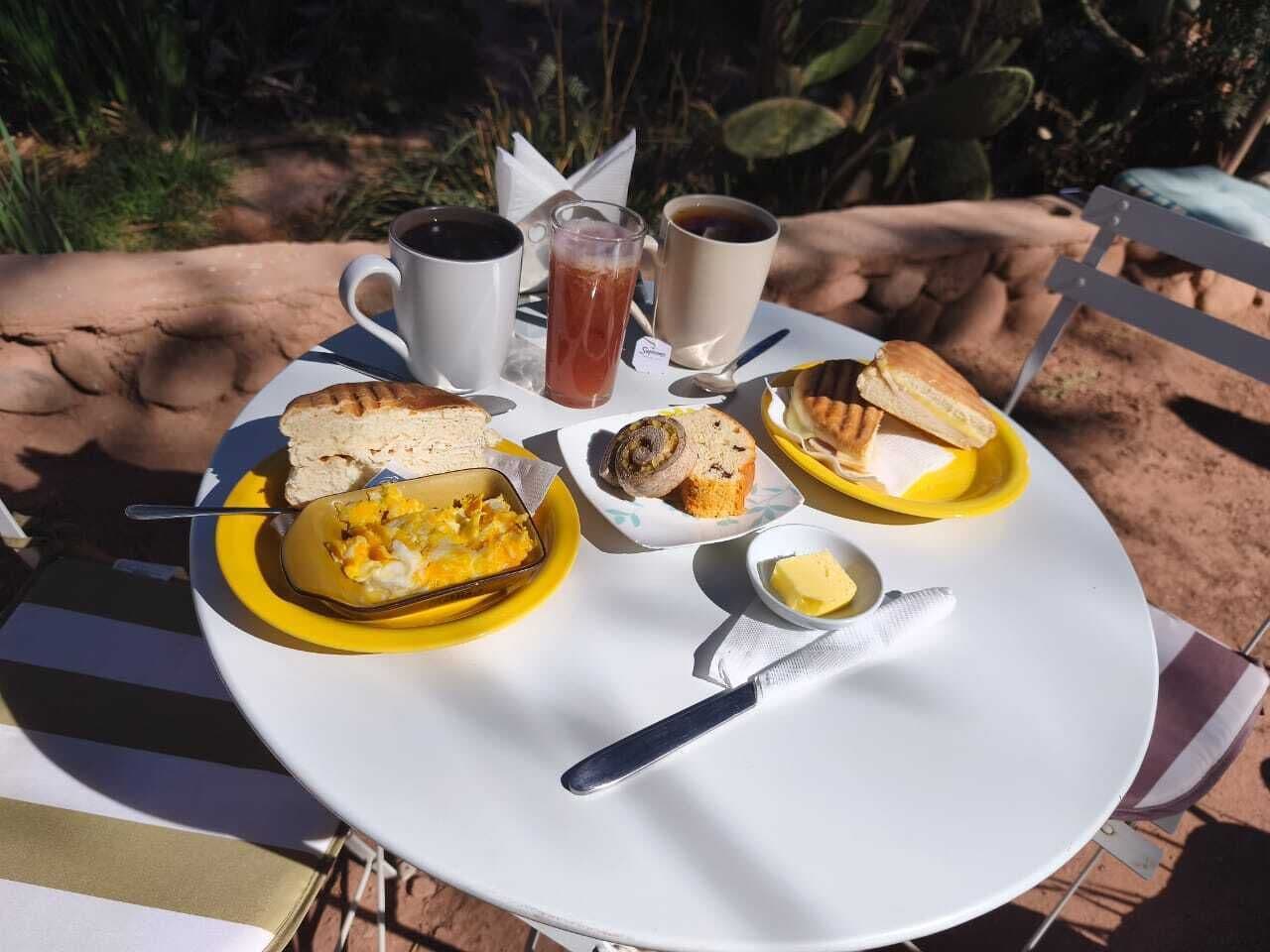 A table set outdoors with a variety of food items and drinks, including sandwiches, eggs, and coffee.
