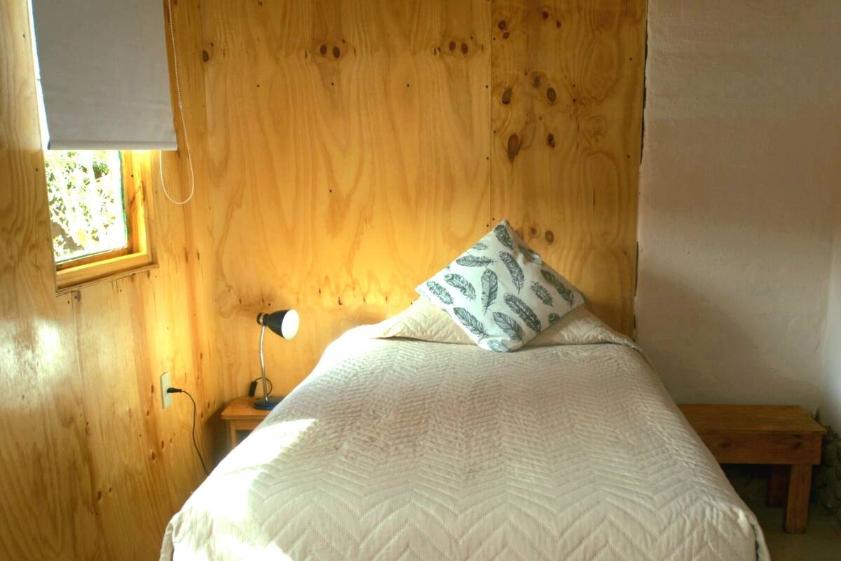 Una habitación de madera con una cama, una mesita de noche y una ventana.