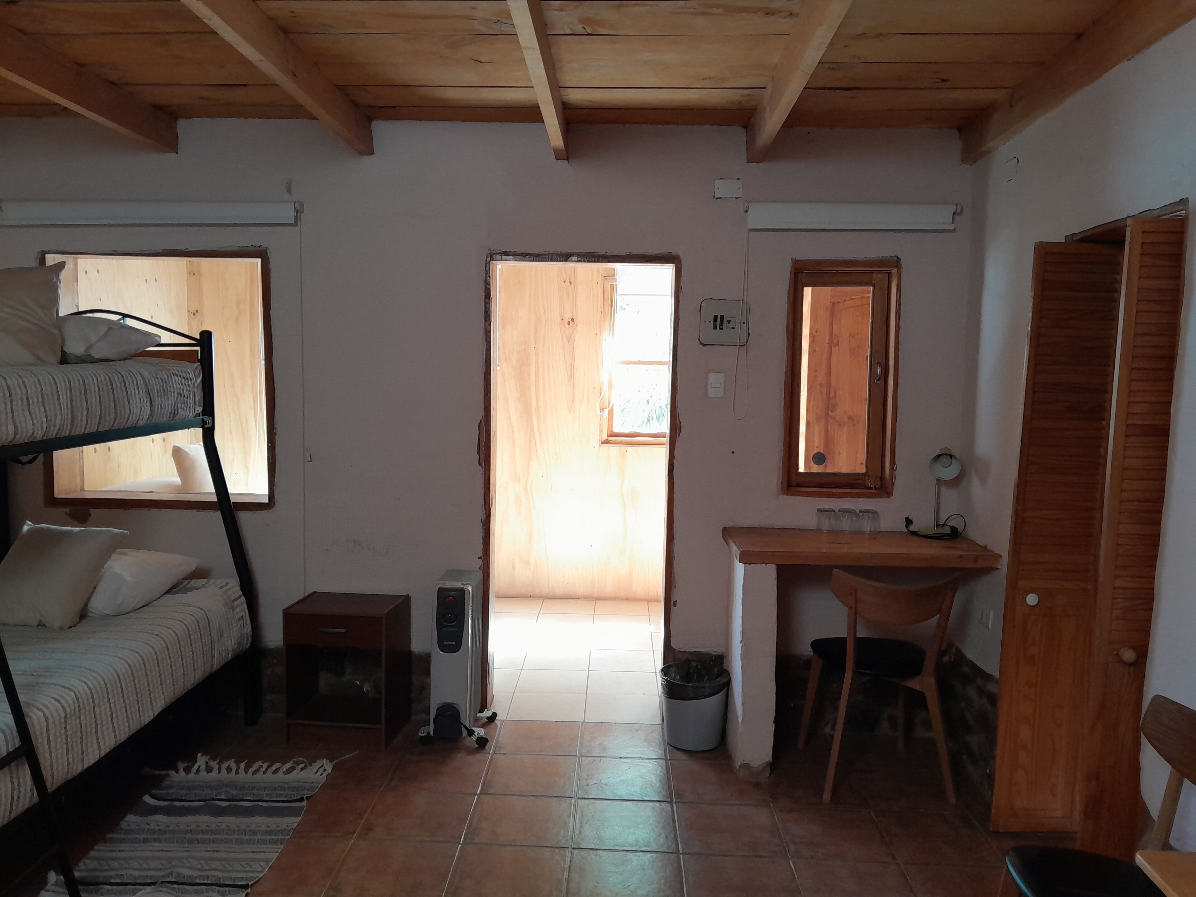 Een kleine kamer met een stapelbed, een bureau, een stoel, een klein tafeltje en een prullenbak.