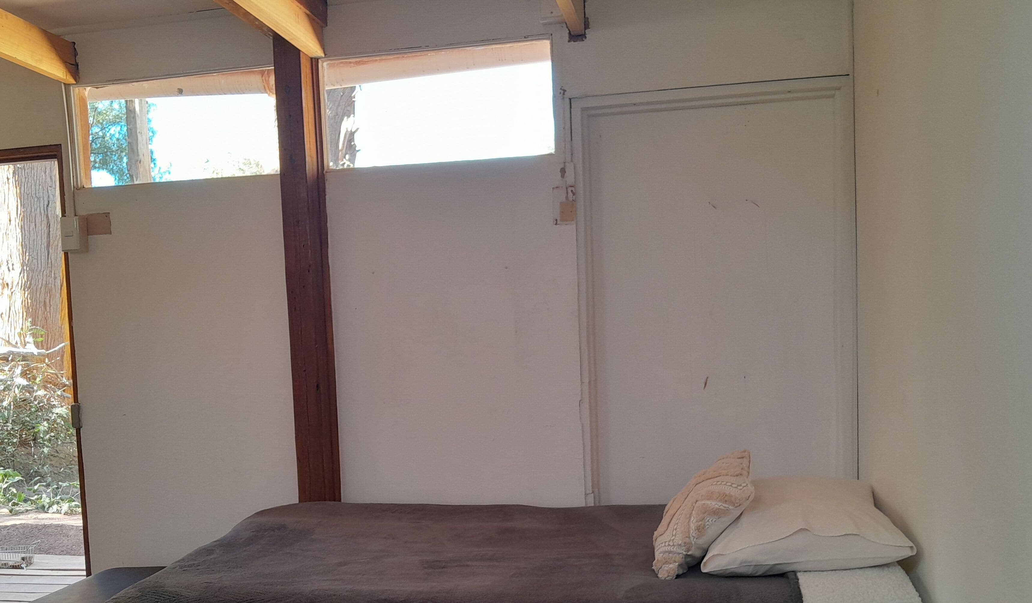 A small, simple room with a single bed, a window, and a door.