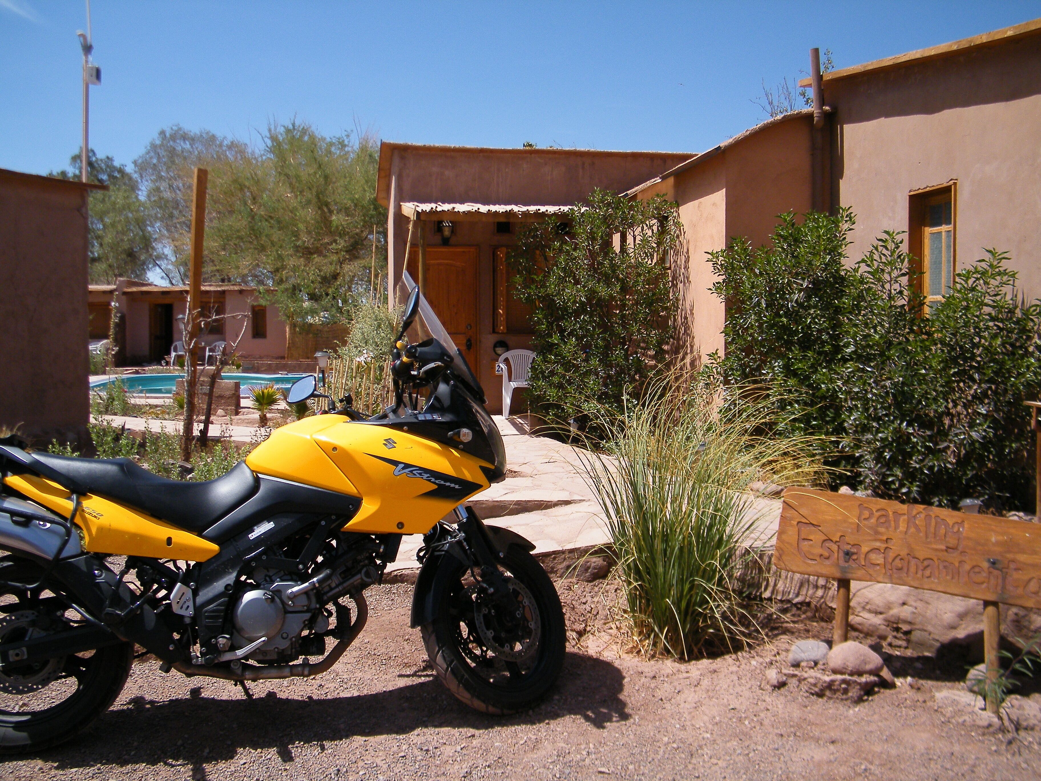 A yellow motorcycle parked in front of a building with a sign that reads "Parking Estacionamiento".