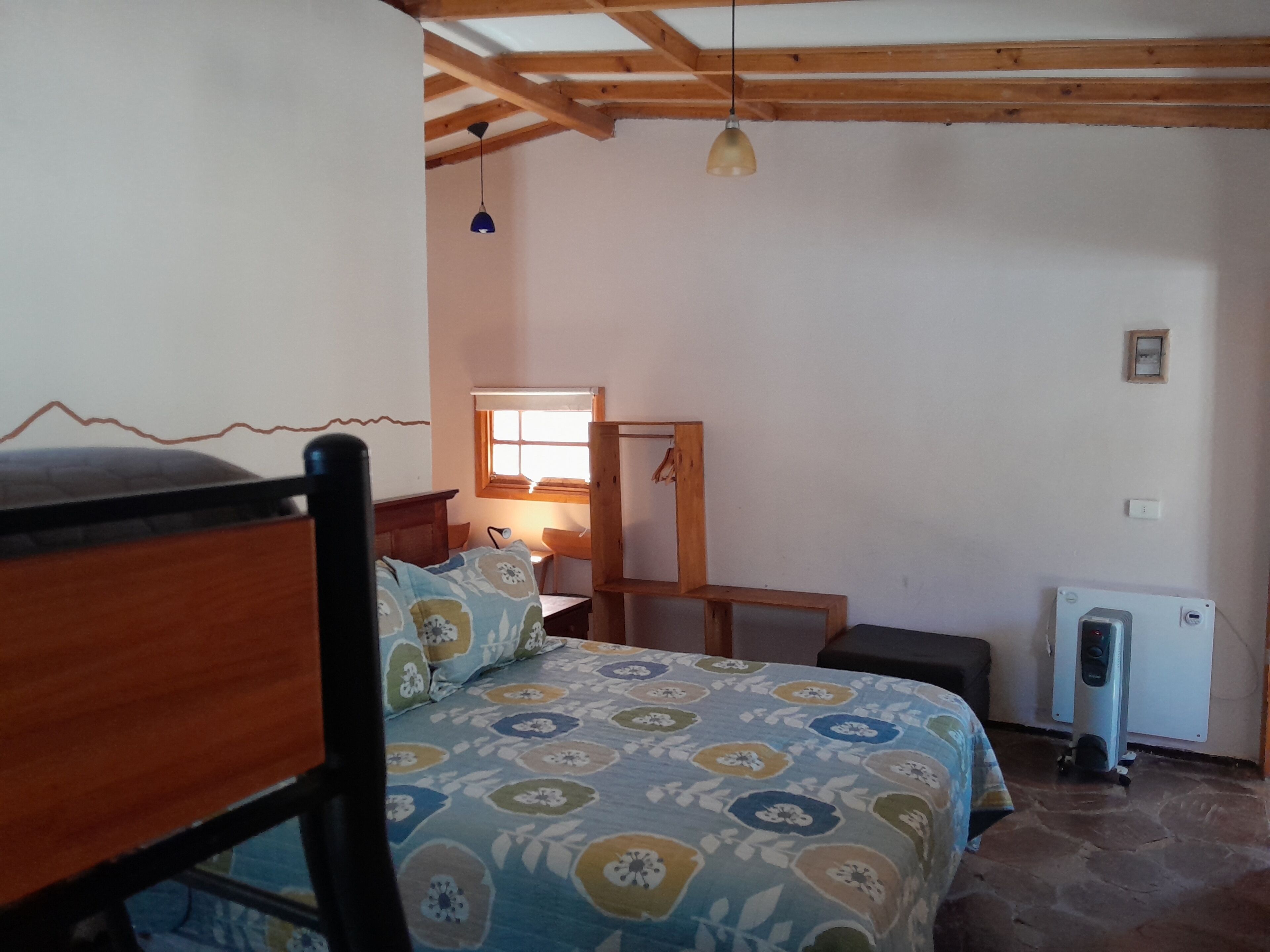 Una camera da letto con un letto, una testiera in legno, una finestra con persiane, una scrivania, una sedia e un termosifone.