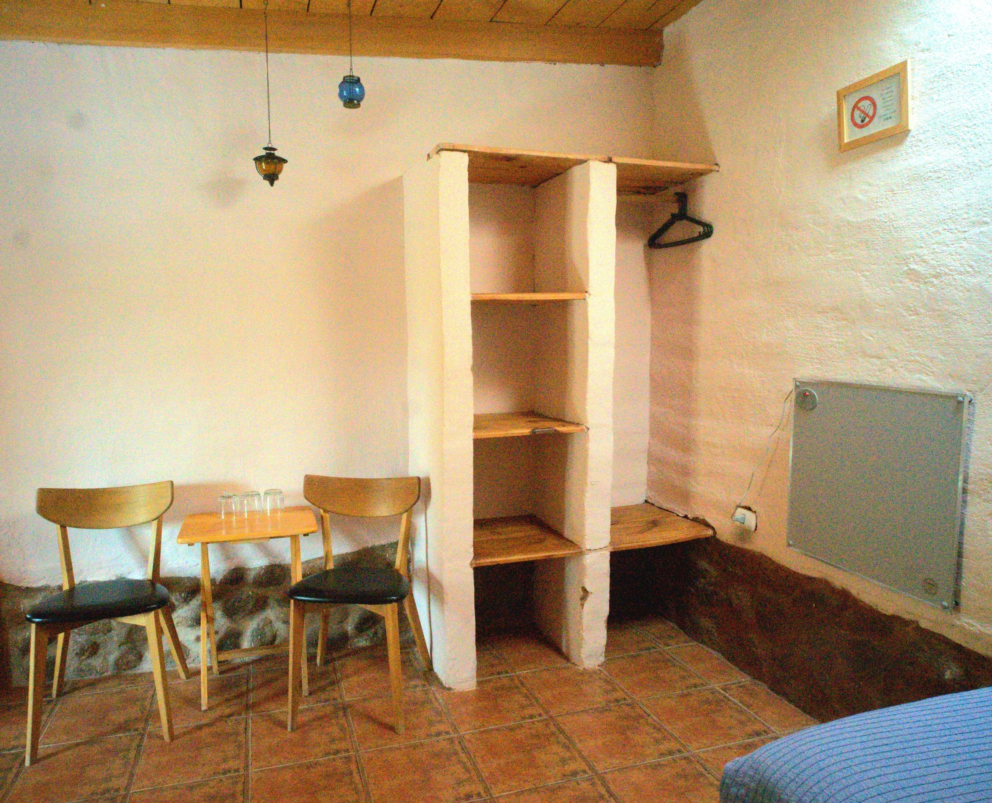Una habitación con una silla de madera, una mesita, un armario y un radiador.
