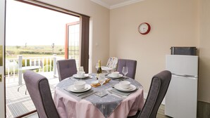 Un coin repas avec une table dressée pour deux personnes, un réfrigérateur et une horloge au mur.