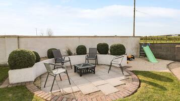 A patio area with a seating arrangement, a fire pit, and a children's play area with a slide.