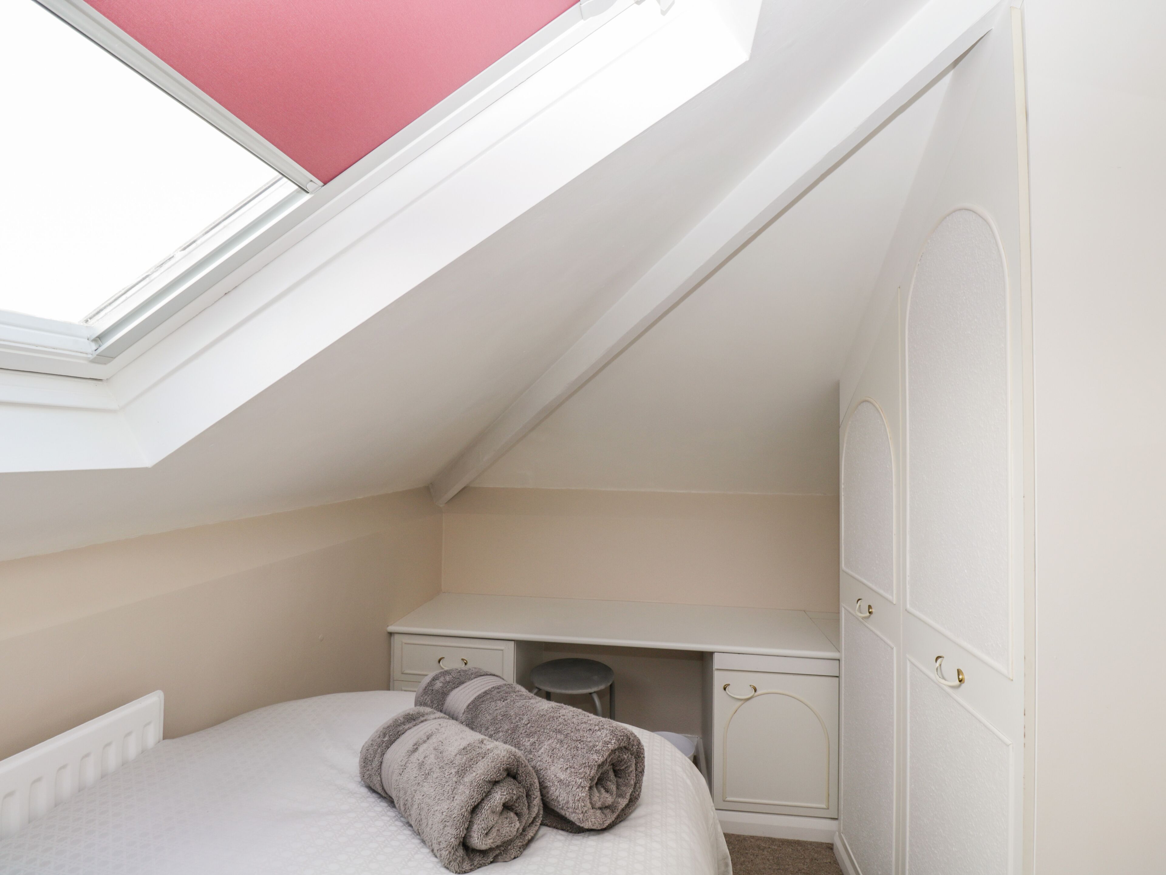 Een kleine, netjes ingerichte slaapkamer met dakraam, een bed, een bureau en een garderobekast.