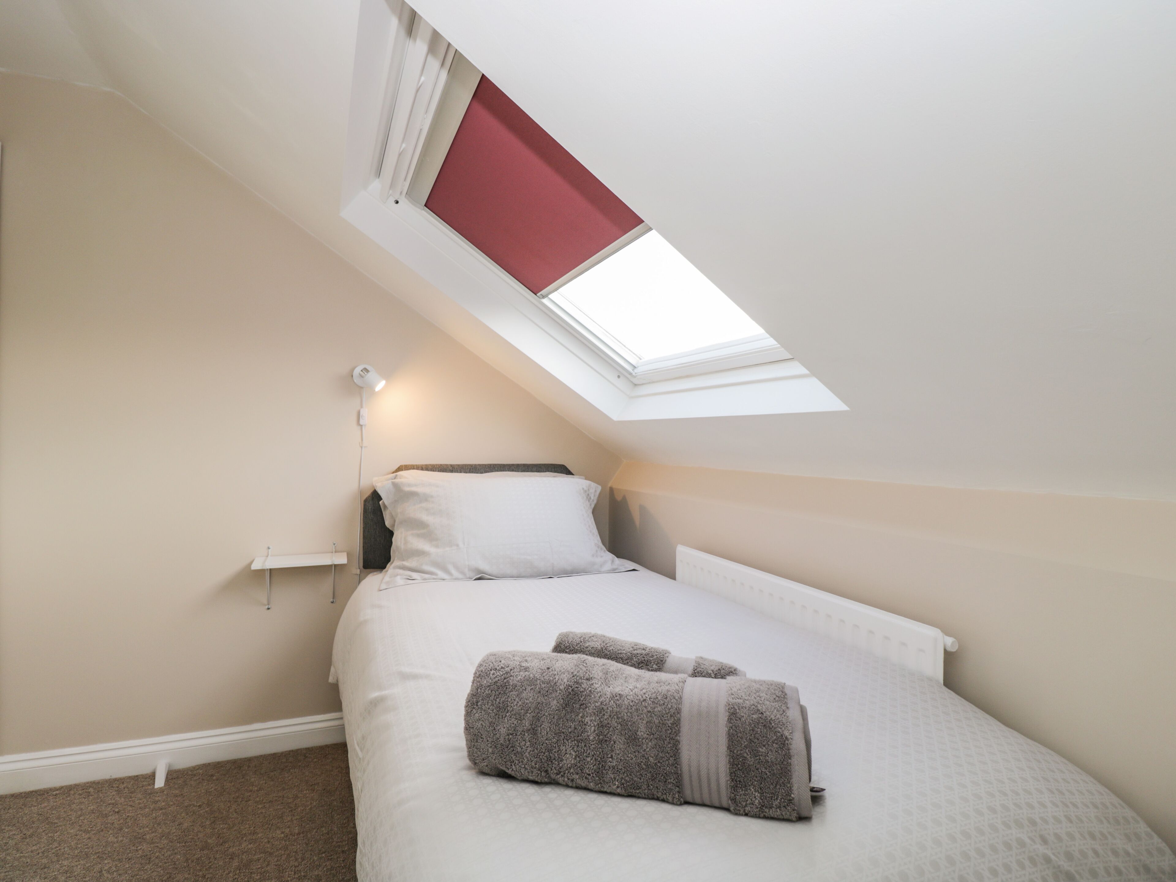A bedroom with a skylight, a bed with white bedding, and a bedside lamp.