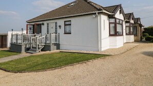 Une maison à deux étages avec un porche à l’avant, une petite terrasse et une allée gravillonnée.