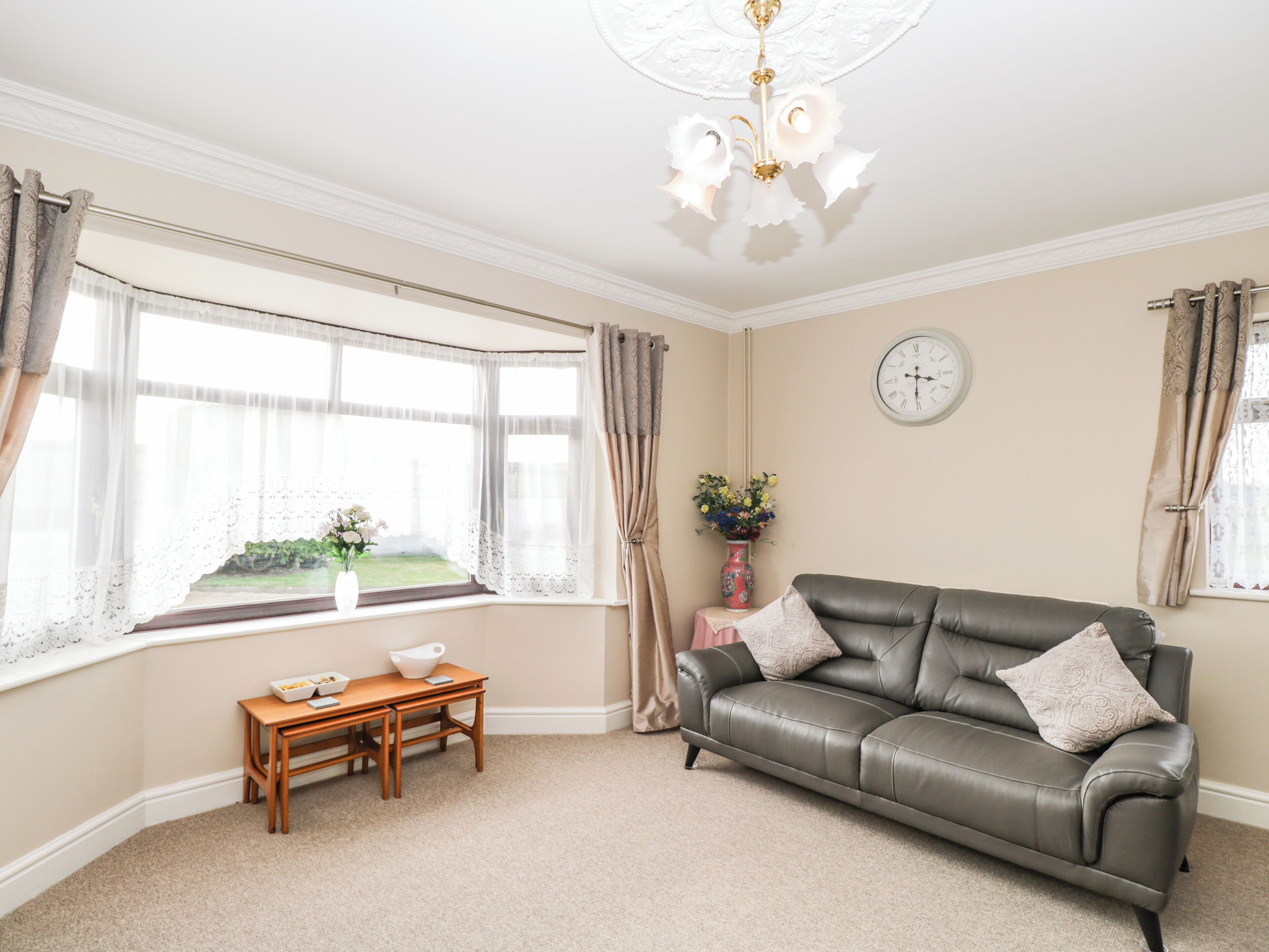 A living room with a leather sofa, a wooden table, a vase with flowers, and a clock on the wall.