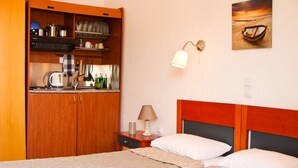 A hotel room with a bed, a wooden wardrobe, a small kitchen area, and a wall-mounted lamp. - Pansion Konstantinos (Skiathos)