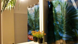 A bathroom with a mirror, a shower curtain with a palm tree design, and a potted plant with orange flowers on a shelf. - Pansion Konstantinos (Skiathos)