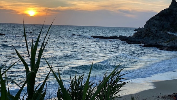 A sunset over a coastal area with waves, a rocky cliff, and some vegetation in the foreground. - Luxury-Unique-Homes 1 Capo Vaticano Tropea (Santa Maria Di Ricadi)