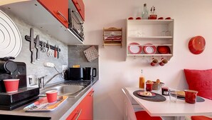 A compact kitchen with red cabinets, a coffee machine, and a dining area with red chairs and a white table.