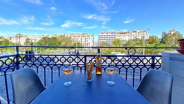 A terrace with a table set for two, featuring a bottle of wine, two glasses, and a vase with breadsticks.