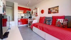 A compact living space with a kitchenette, a dining area, and a bed with red bedding.