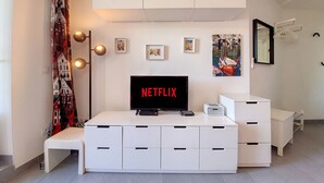 A modern living room with a white entertainment unit, a flat-screen TV displaying 'NETFLIX', a bench, and a patterned curtain.