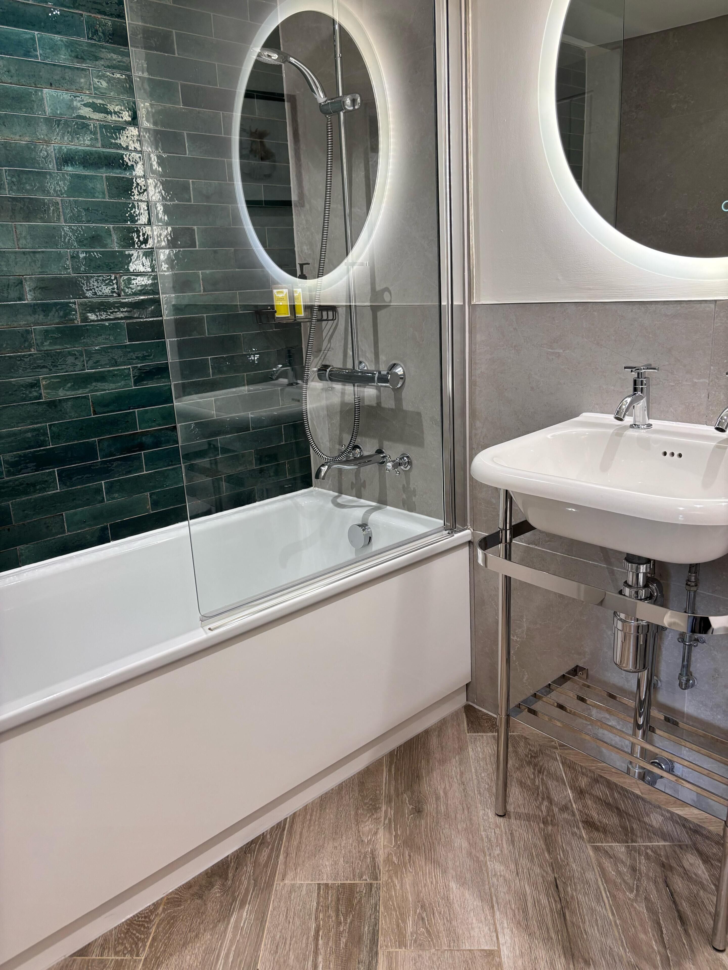 A modern bathroom with a glass-enclosed bathtub, a white sink, and a large mirror.
