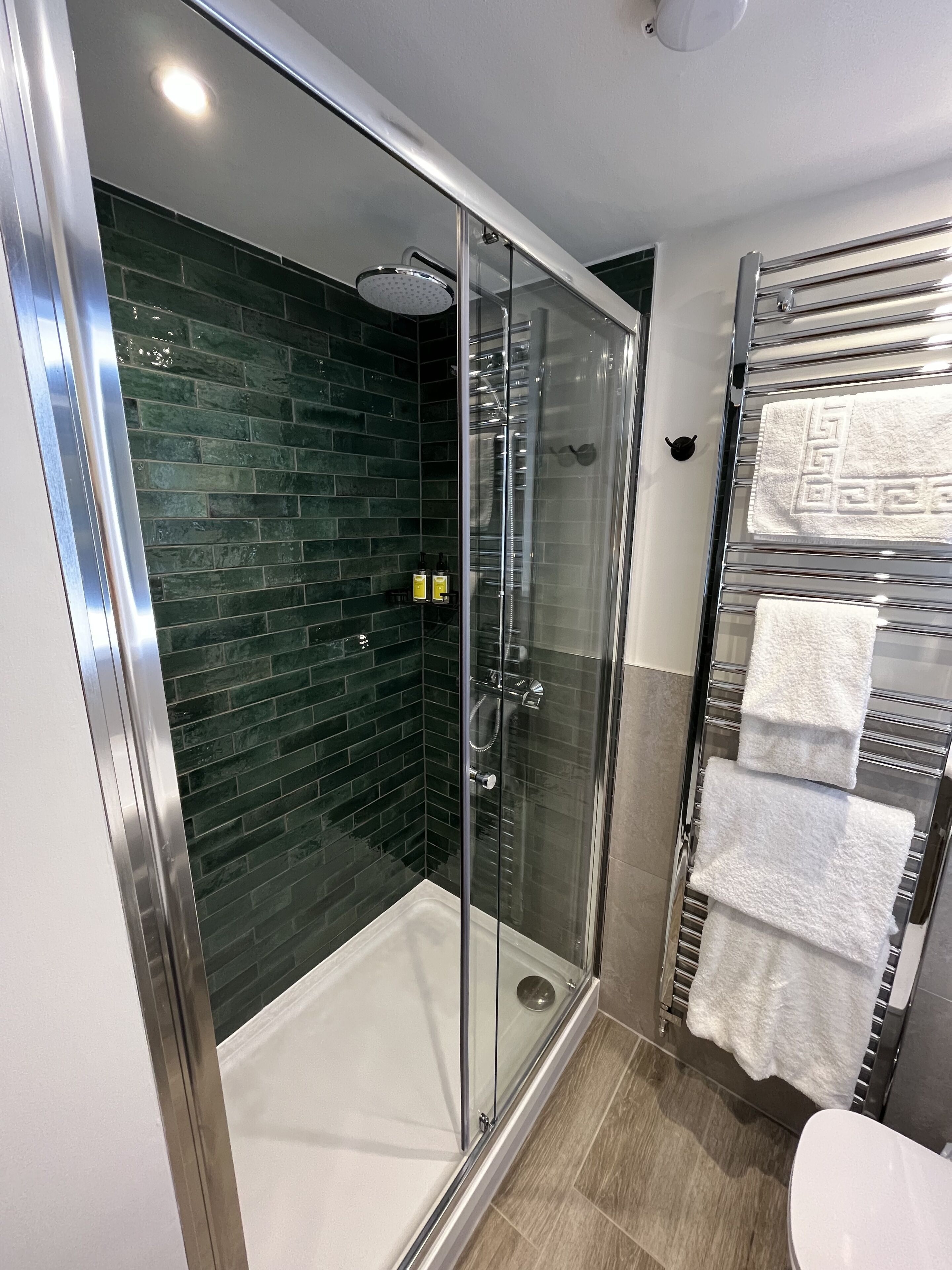 A modern bathroom with a glass-enclosed shower, dark green tiled walls, and a glass shower door.