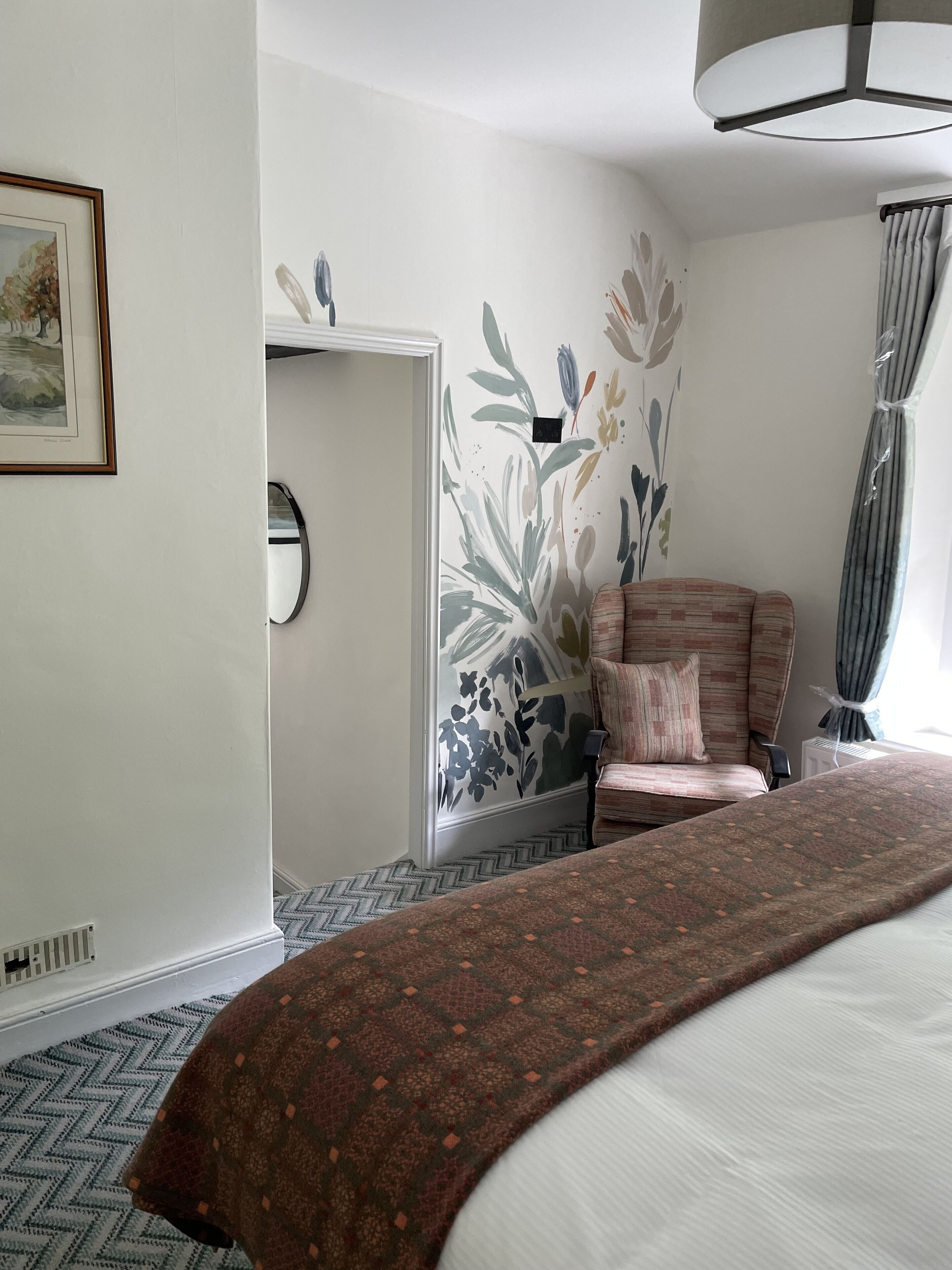 Ein Hotelzimmer mit einem Bett, einem Sessel, einem Spiegel und einer Wand mit floralem Wandbild.
