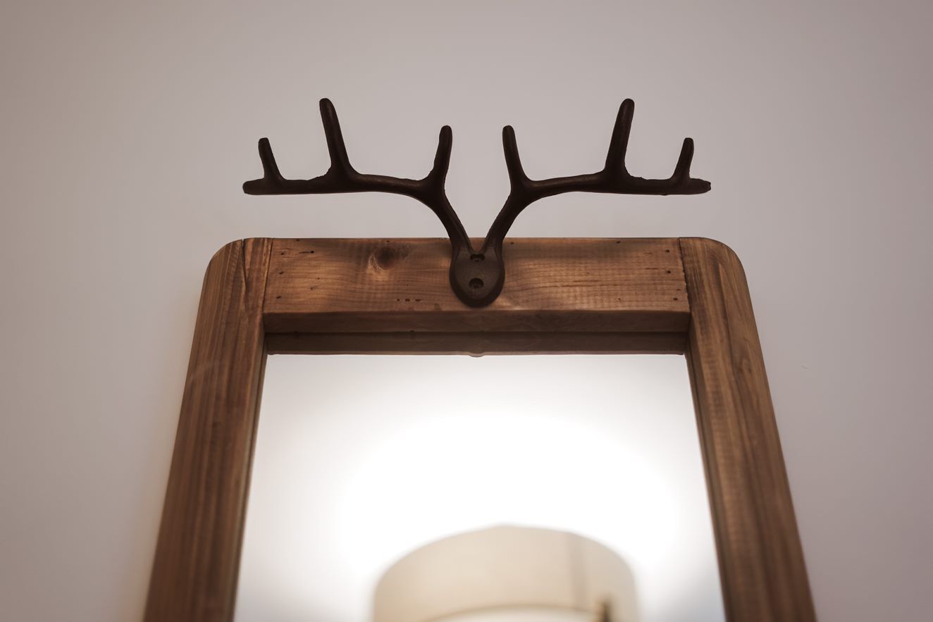 A wooden-framed mirror with a deer antler-shaped wall mount.