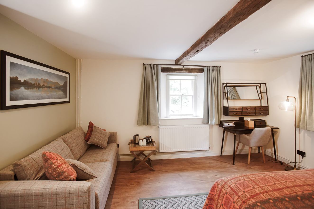 A cozy room with a wooden floor, a sofa, a desk with a chair, a radiator, and a window with curtains.