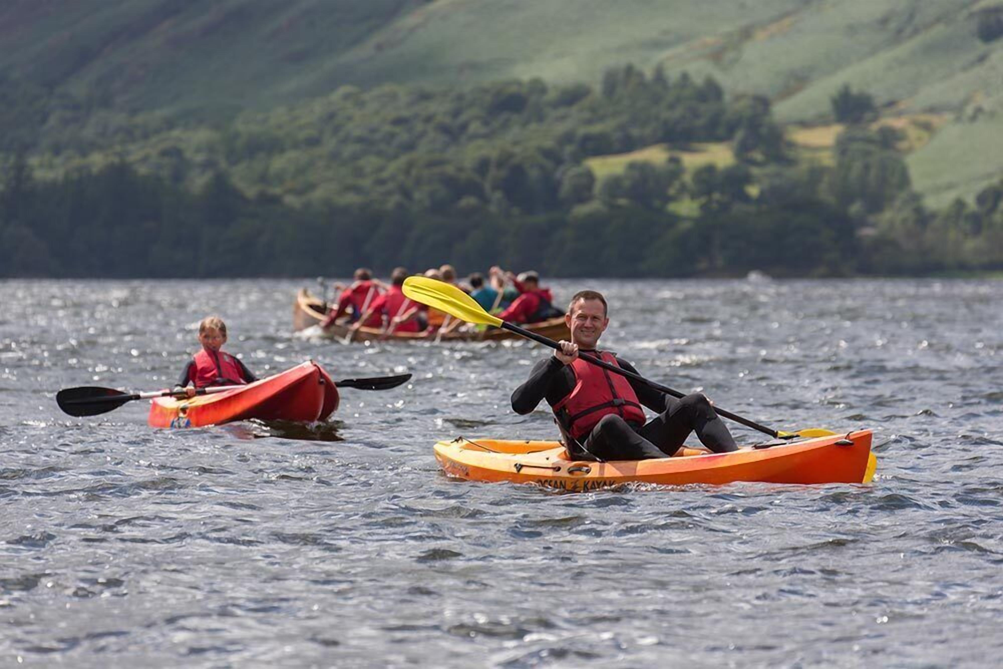 Un groupe de personnes pratiquant le kayak sur un lac, avec une chaîne de montagnes en arrière-plan.