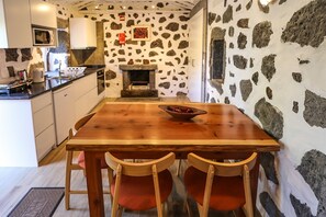 A rustic kitchen with stone walls, a wooden dining table, and red upholstered chairs.