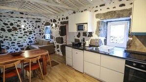 Een keuken met stenen muren, een houten eettafel en witte kastjes.