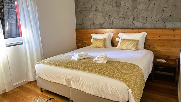 Een hotelkamer met een groot bed, een houten hoofdbord en een stenen muur.