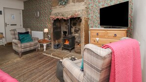 A cozy living room with a stone fireplace, a television, and a patterned wallpaper. - Penistone View (Keighley)