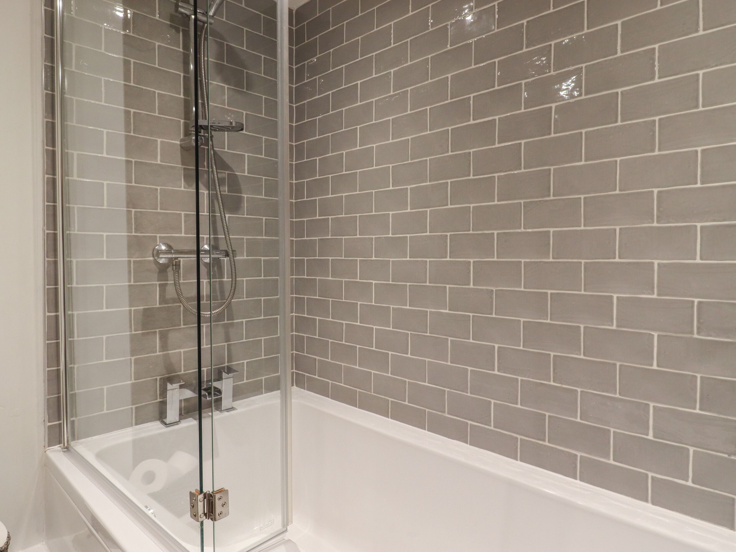 Un baño moderno con ducha de vidrio, una bañera blanca y paredes cubiertas de azulejos grises.
