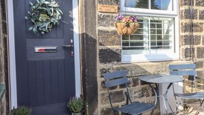 A stone building with a dark blue door, a hanging flower basket, a small table with chairs, and a sign reading "Penistone View". - Penistone View (Keighley)