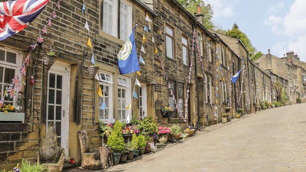 A row of traditional stone buildings with flags and potted plants. - Penistone View (Keighley)