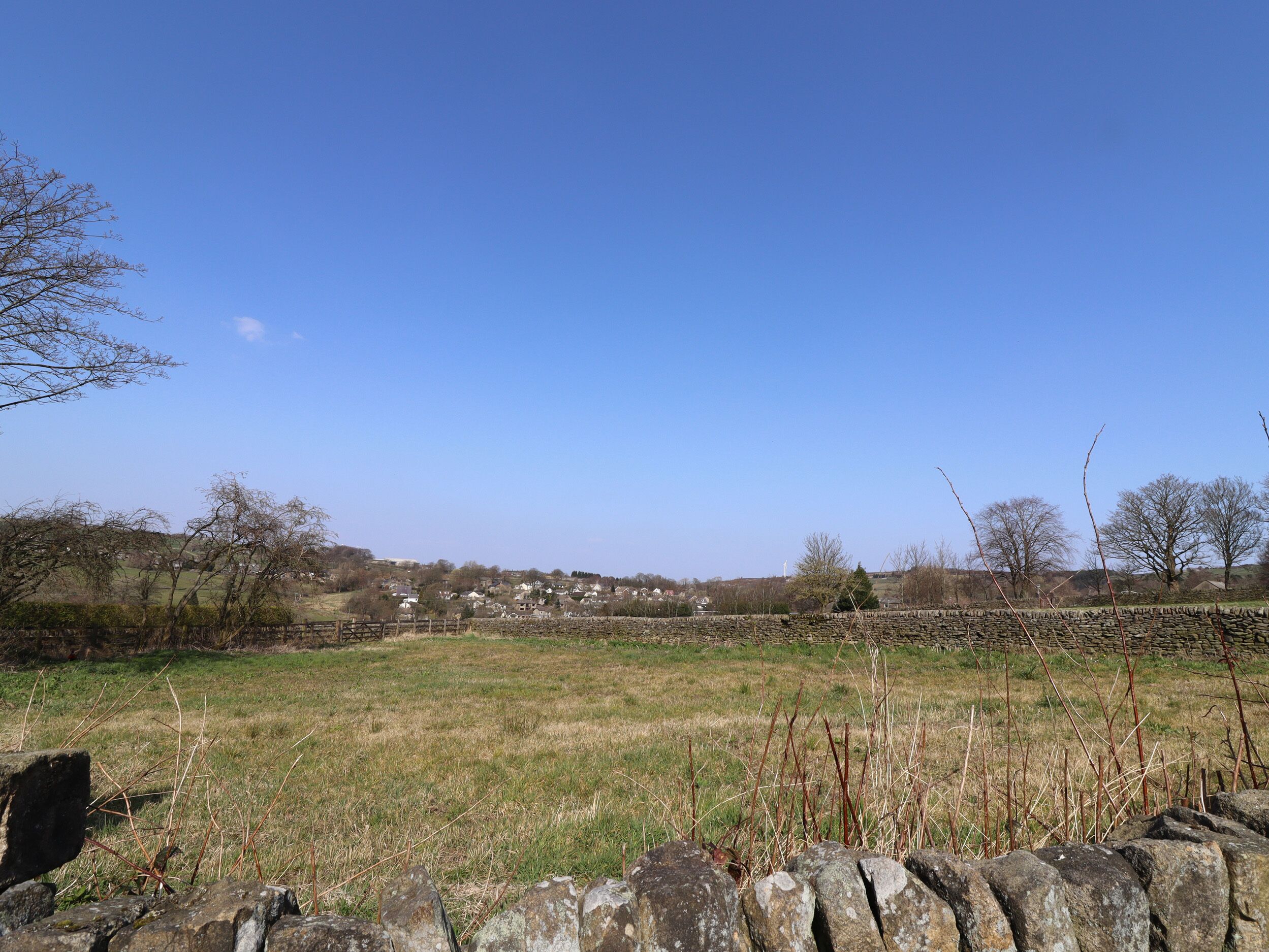 A rural landscape with stone walls, a clear sky, and distant buildings.