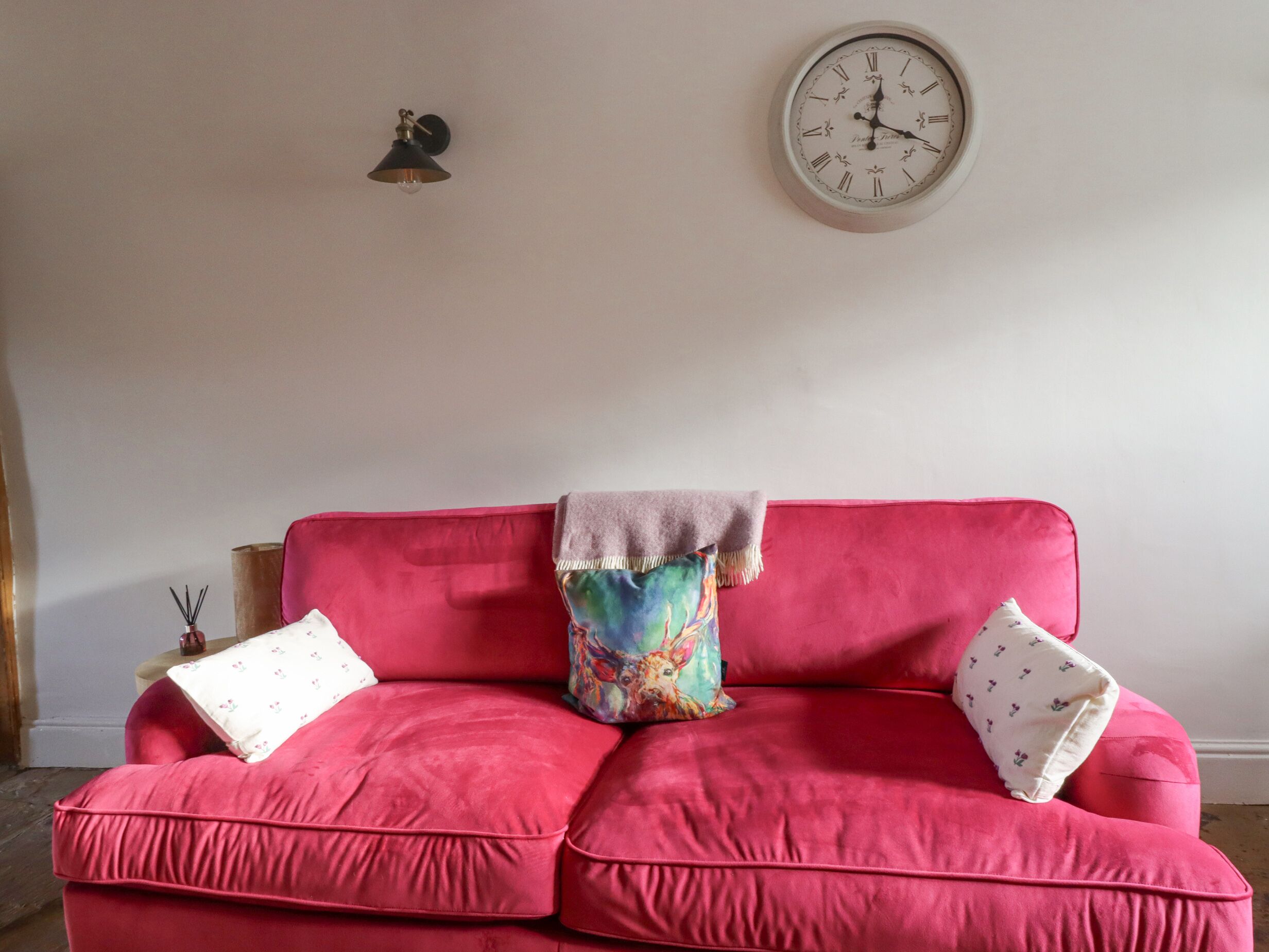 A red sofa with two pillows, a colorful throw blanket, and a wall clock.