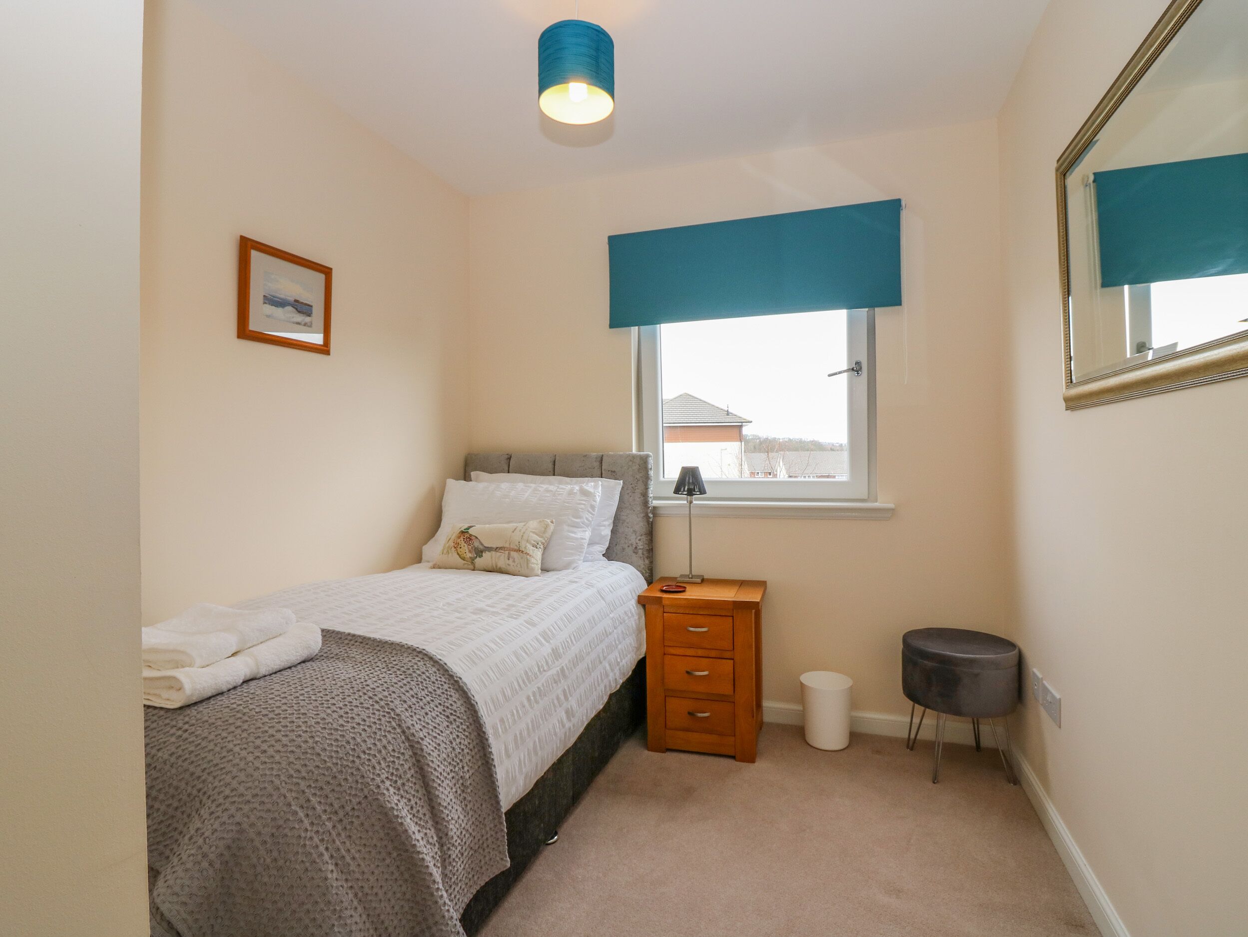 A bedroom with a bed, a bedside table, a lamp, a mirror, and a window with a view of buildings outside.