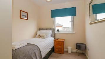 A bedroom with a bed, a bedside table, a lamp, a mirror, and a window with a view of buildings outside.